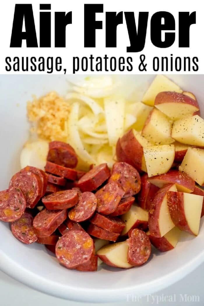 Sliced air fryer sausage, chopped red potatoes, and sliced onions in a white bowl, ready for air frying.