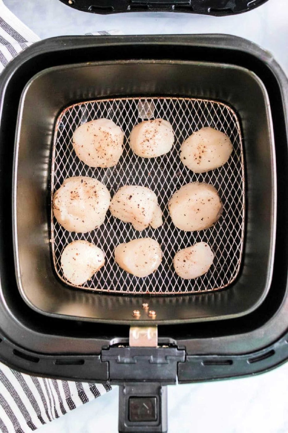 Air fryer scallops are seasoned with pepper and arranged in a single layer inside the air fryer basket for solid, tender results.
