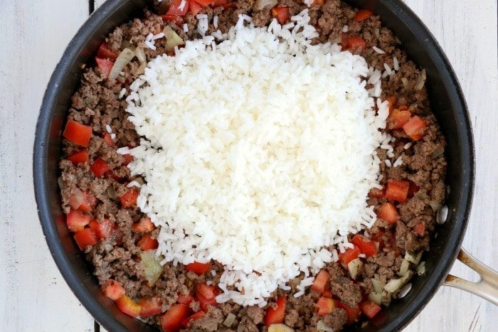 A skillet with cooked ground beef, chopped tomatoes, and a mound of white rice on top—solid ingredients for making air fryer stuffed peppers.