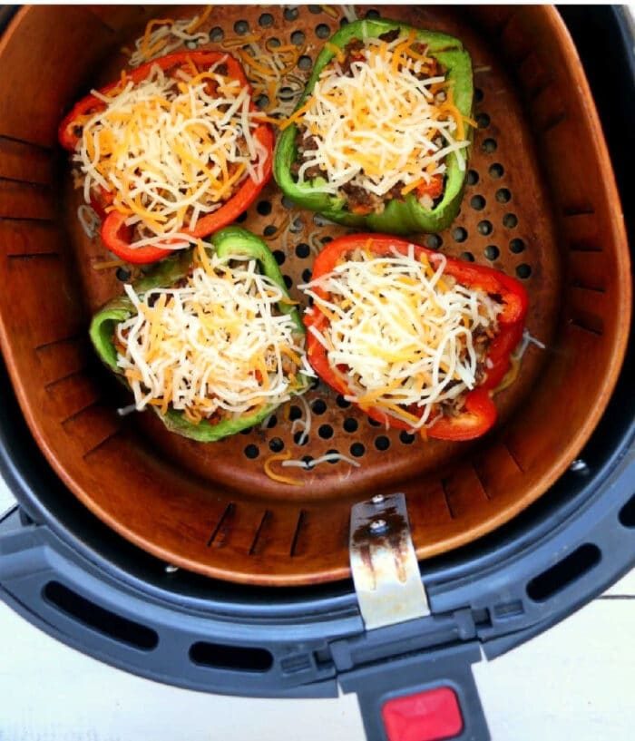 Four halved bell peppers filled with ground meat and shredded cheese make good air fryer stuffed peppers, arranged perfectly in the air fryer basket.