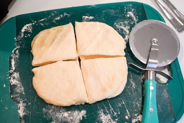 Homemade flour tortilla recipe in its simplicity, is cut into four pieces on a green cutting board, with a pizza cutter resting beside it.