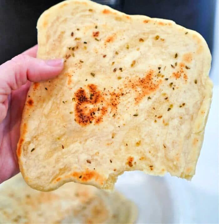 A hand holds a piece of tortilla, richly adorned with herbs and spices, reminiscent of homemade air fryer tortillas.