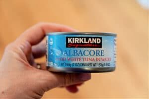 A hand holds a can of Kirkland Signature Albacore Solid White Tuna in Water, solid for pairing with crockpot chicken dishes made from frozen breasts.