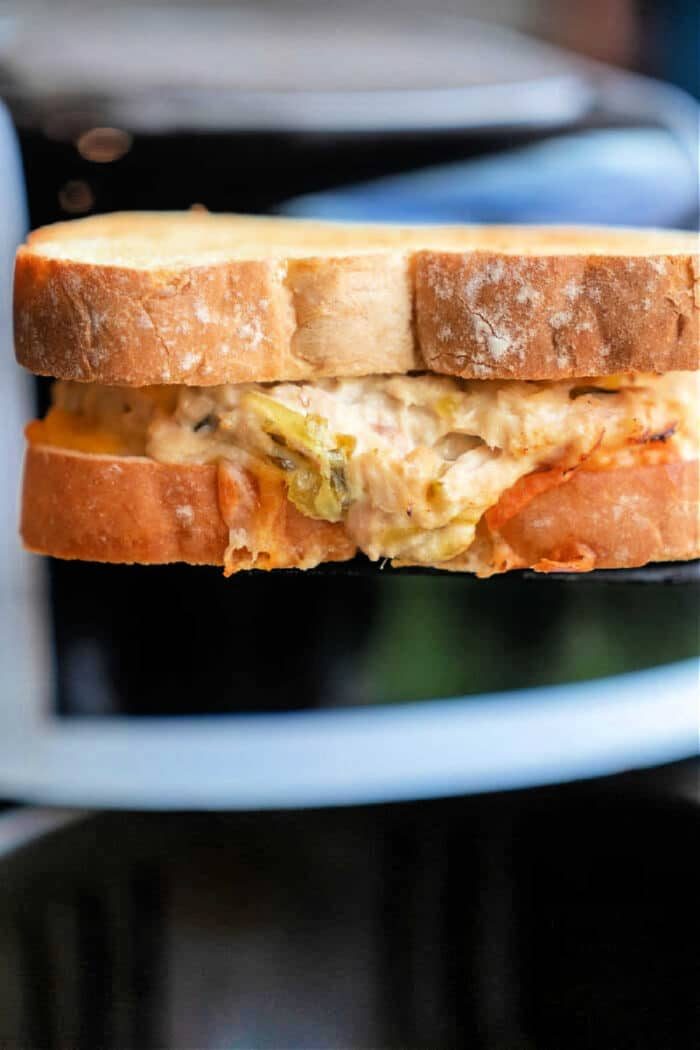 A close-up of a toasted air fryer tuna melt. The bread is golden brown, with the good filling peeking from the bitten corner.