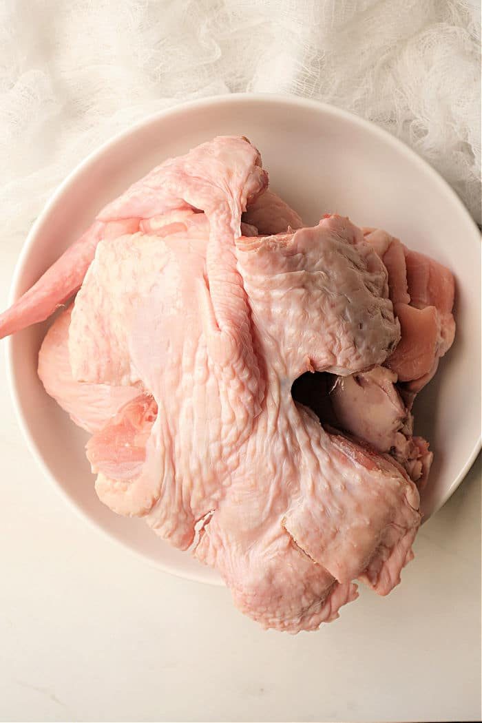 A bowl containing raw turkey wings is placed on a light-colored surface, with a white textured fabric in the background.