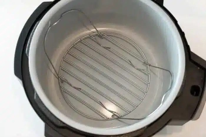 The image shows the interior of an empty electric pressure cooker, ready to prepare good meals like an air fryer whole chicken. The metal insert and cooking rack are visible, and the pot is clean with a stainless steel inner surface and a black exterior casing.