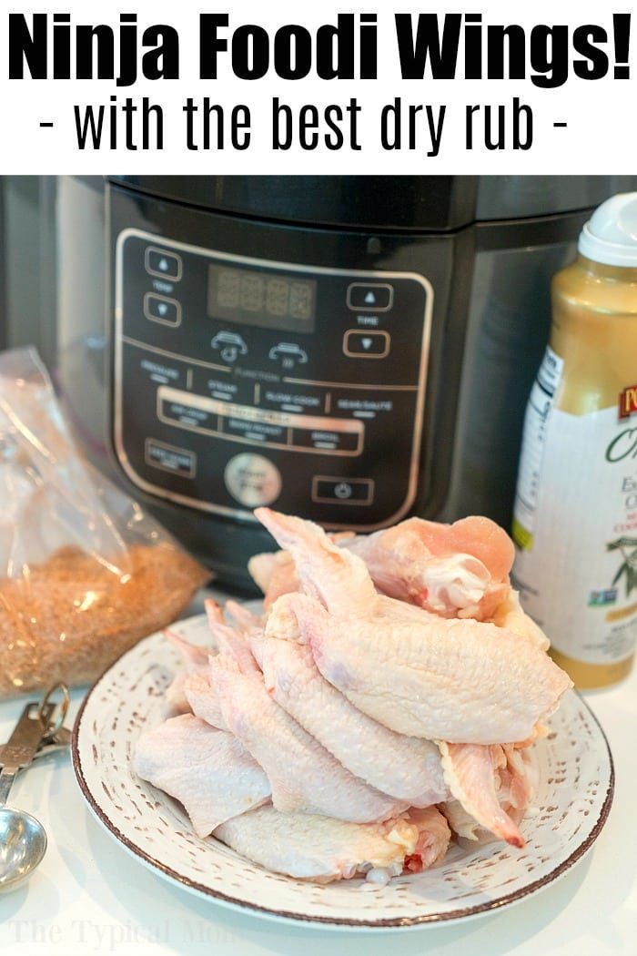 A plate of raw chicken wings awaits the Ninja Foodi air fryer, ready to become the ultimate air fryer wings recipe. A packet of seasoning and a bottle of mustard sit nearby, promising flavor perfection. The text above reads, "Ninja Foodi Wings! - with the best dry rub -".