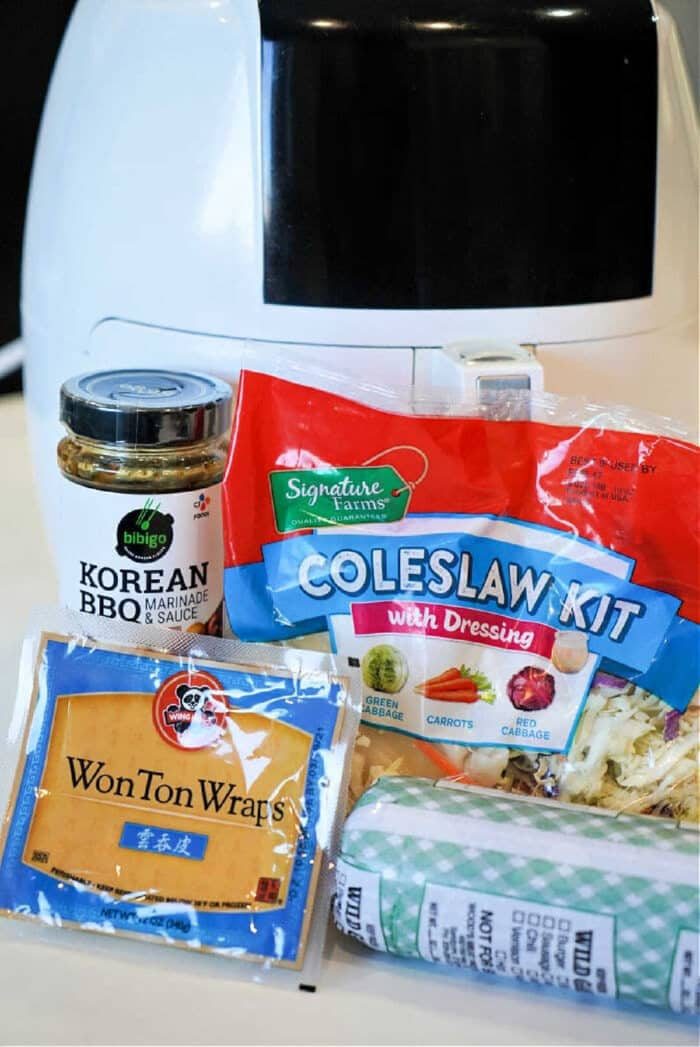 A jar of Korean BBQ sauce, coleslaw kit, wonton wraps, and ground pork in front of an air fryer—solid for making flavorful air fryer won tons at home.