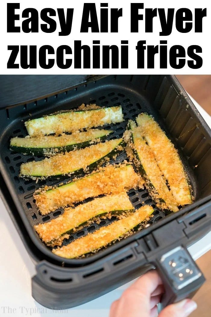 A close-up of air fryer zucchini fries coated in breadcrumbs cooking in an air fryer basket. The text at the top reads "Easy Air Fryer zucchini fries," and a hand is shown holding the air fryer drawer.