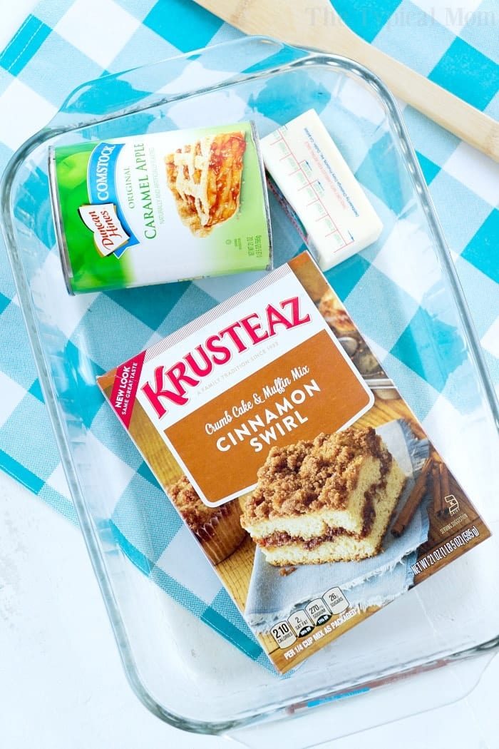Box of Krusteaz cinnamon swirl mix, caramel apple pie filling, and butter in a glass baking dish on a blue checkered cloth—solid for making an easy apple spice dump cake.