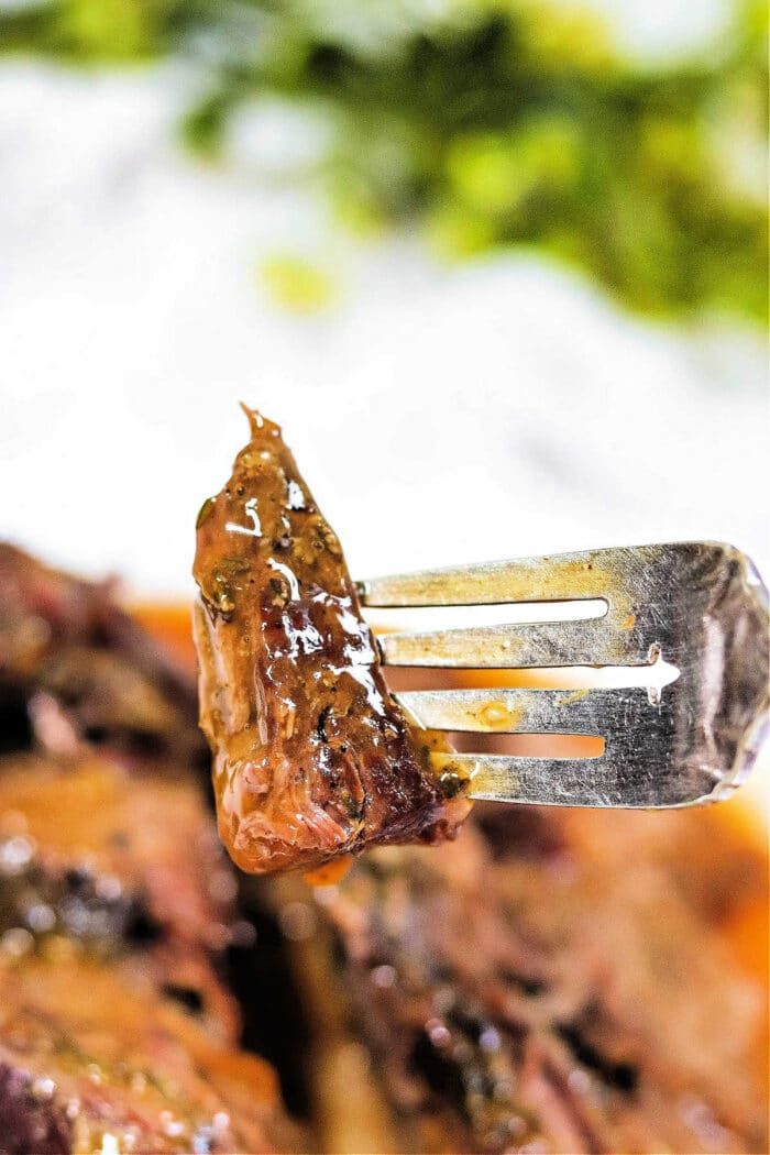 A close-up of a fork holding a juicy, glazed piece of arm roast with herbs—a good result from a slow cooker.