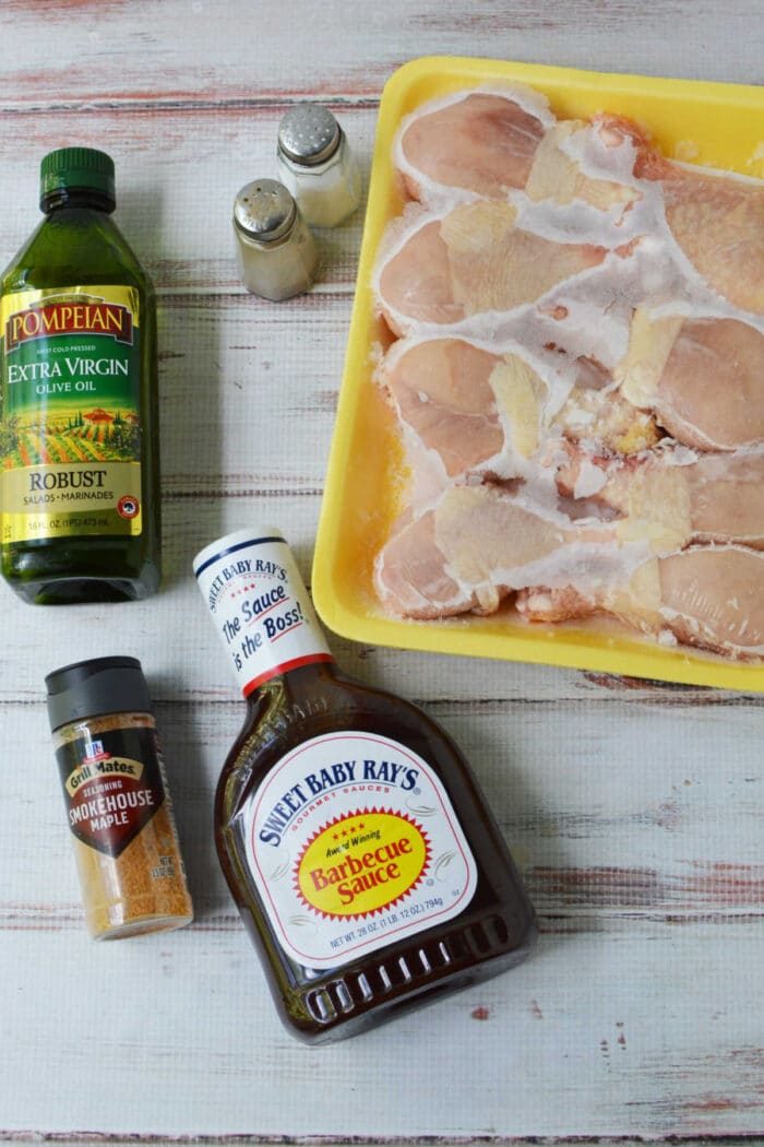 Raw chicken legs in a yellow tray with olive oil, barbecue sauce, seasoning, and salt and pepper shakers—everything you need to prepare good baked chicken legs or use frozen chicken legs for a quick and easy meal.