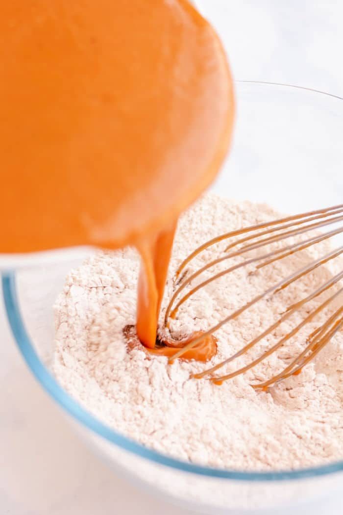 pumpkin being poured into a bowl of dry ingredients with a whisk, creating the solid base for baked pumpkin donuts.