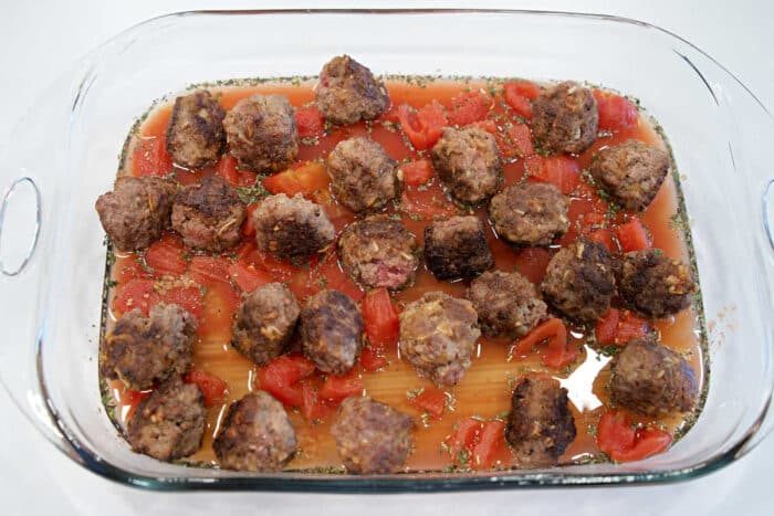 Baking dish with meatballs, diced tomatoes, sauce, and herbs, arranged over uncooked lasagna noodles for a good twist on Baked Spaghetti with Meatballs.