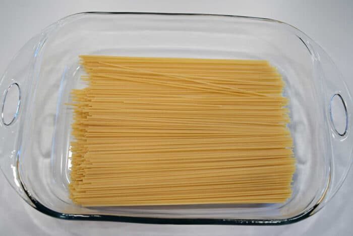 Uncooked spaghetti noodles arranged in a clear glass baking dish on a white surface, ready to be transformed into good baked spaghetti with meatballs.
