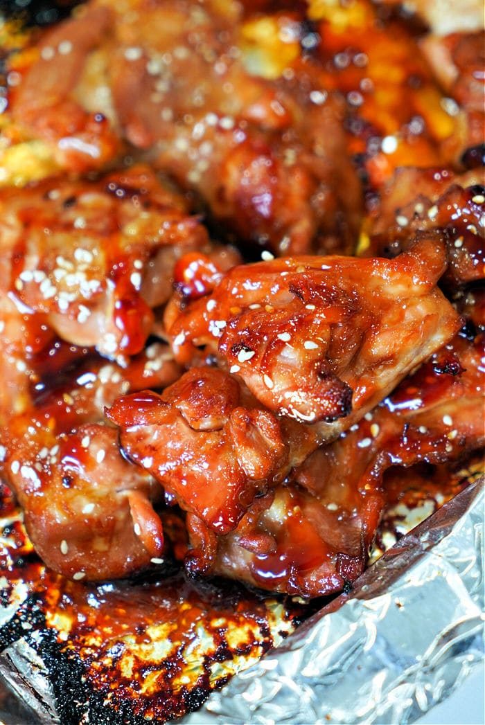 Close-up of teriyaki glazed, baked teriyaki chicken thighs sprinkled with sesame seeds on a foil-lined tray.
