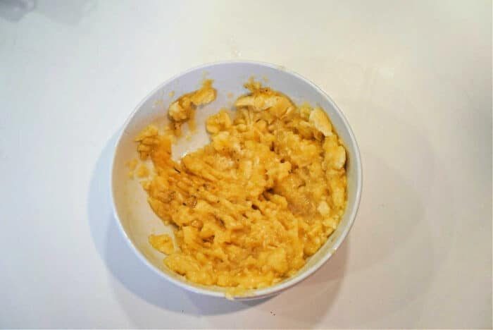 White bowl filled with mashed bananas, solid for topping your Bananas and Cream Oatmeal, on a white surface.