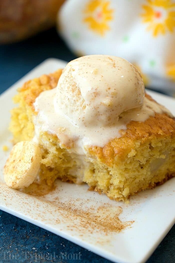 A slice of banana cake topped with a scoop of vanilla ice cream rests elegantly on a white square plate, evoking the comforting flavors of banana pudding.
