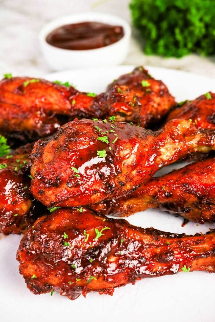 Oven baked BBQ chicken legs glazed with barbecue sauce and garnished with herbs, served on a white plate with sauce in the background—a flavorful chicken recipe solid for any occasion.