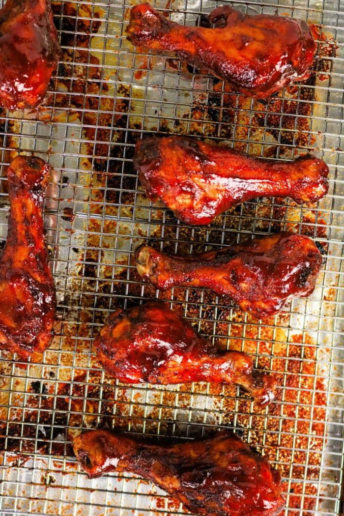 Seven glazed BBQ chicken legs on a wire rack over a baking sheet, coated in rich barbecue sauce for the solid baked BBQ chicken delight.