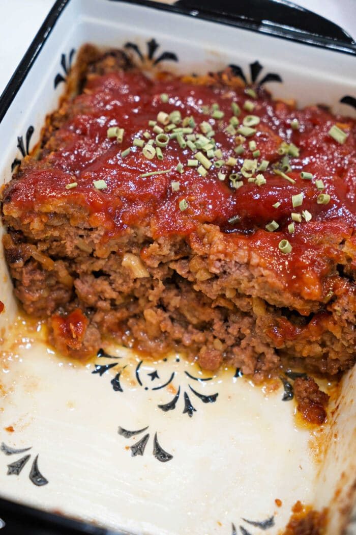 A sliced meatloaf topped with tomato sauce and herbs in a white baking dish with a black pattern, solid for trying a classic Meatloaf Recipe or transforming into a savory BBQ Meatloaf.