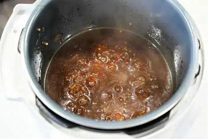 A close-up of a steaming pot in instant pot reveals a dark, bubbling gravy brimming with spices. The well-worn pot cradles a savory beef arm roast recipe, its contents simmering energetically.