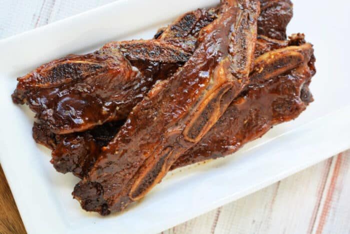 Grilled beef riblets with a shiny glaze, served on a rectangular white plate—a mouthwatering beef recipe solid for any occasion.
