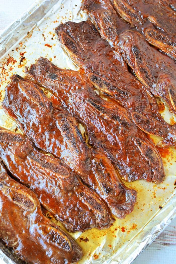 Rows of glazed, cooked beef riblets rest on a foil-lined baking sheet—solid for anyone searching for a savory beef riblets recipe.