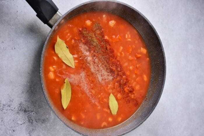 A pan of tomato sauce with beans, bay leaves, and spices on a light gray surface—solid as a base if you're exploring how to cook beef shin in oven for a rich, hearty meal.