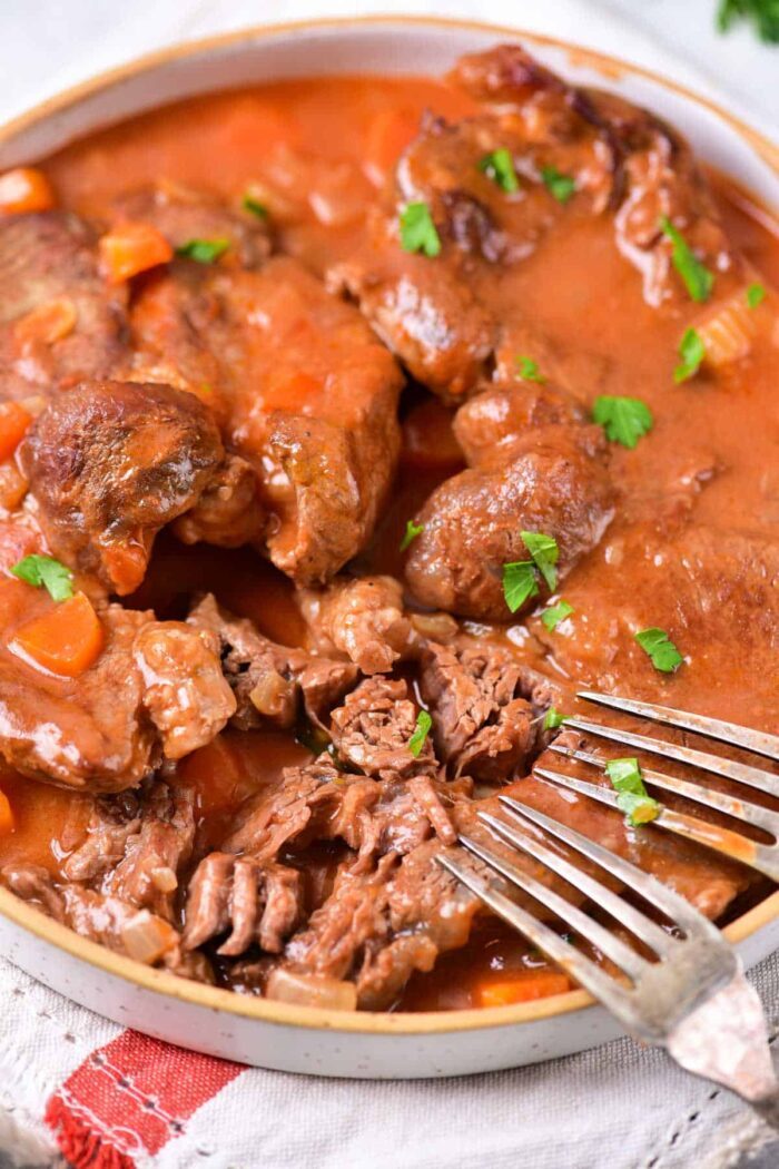 Beef pot roast in tomato sauce, garnished with parsley—a tender Beef Shin recipe ready to shred.