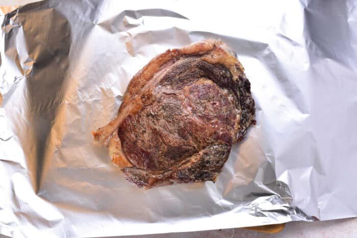 A cooked steak resting on a sheet of crumpled aluminum foil, out of the oven—an appetizing result when learning how to cook beef strip steak in the oven to perfection.