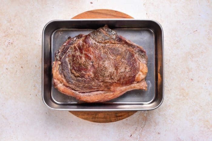 Cooked strip steak in a metal roasting pan on a round wooden board, viewed from above—solid inspiration if youre wondering how to cook beef strip steak in the oven for juicy and good results.