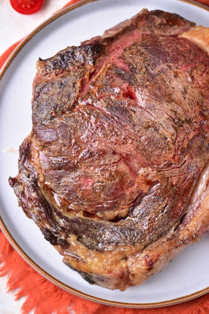 A cooked steak with a seared crust, served on a white plate with an orange placemat underneath—solid inspiration if you're wondering how to cook beef strip steak in the oven for a similar juicy result.