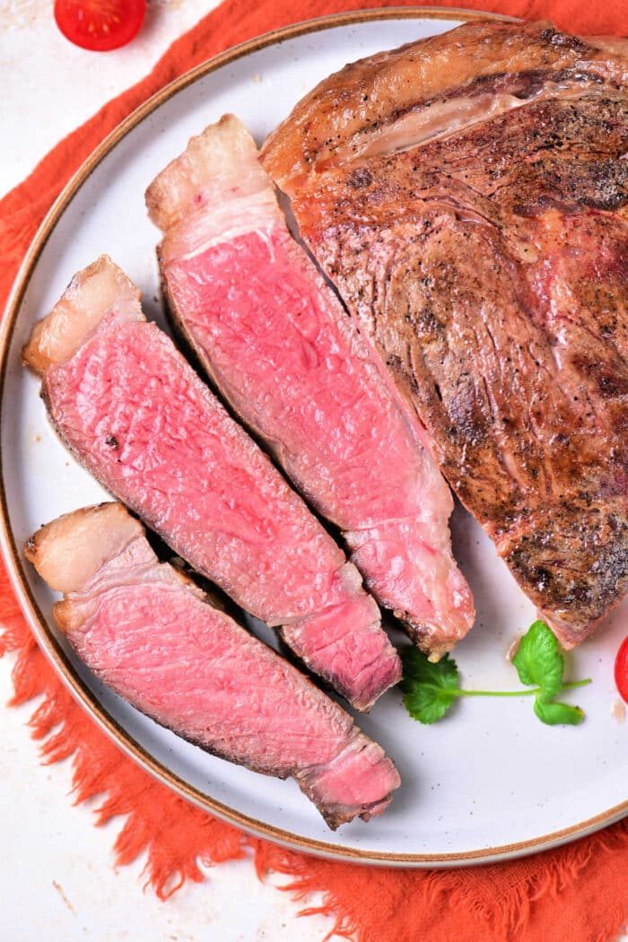 Sliced medium-rare steak on a white plate with a red napkin underneath, solid for showcasing the results of learning how to cook beef strip steak in the oven.