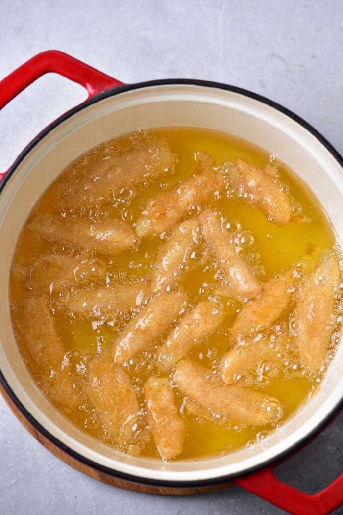 Golden french fries frying in a red pot with bubbling oil, reminiscent of crispy beer batter fries.