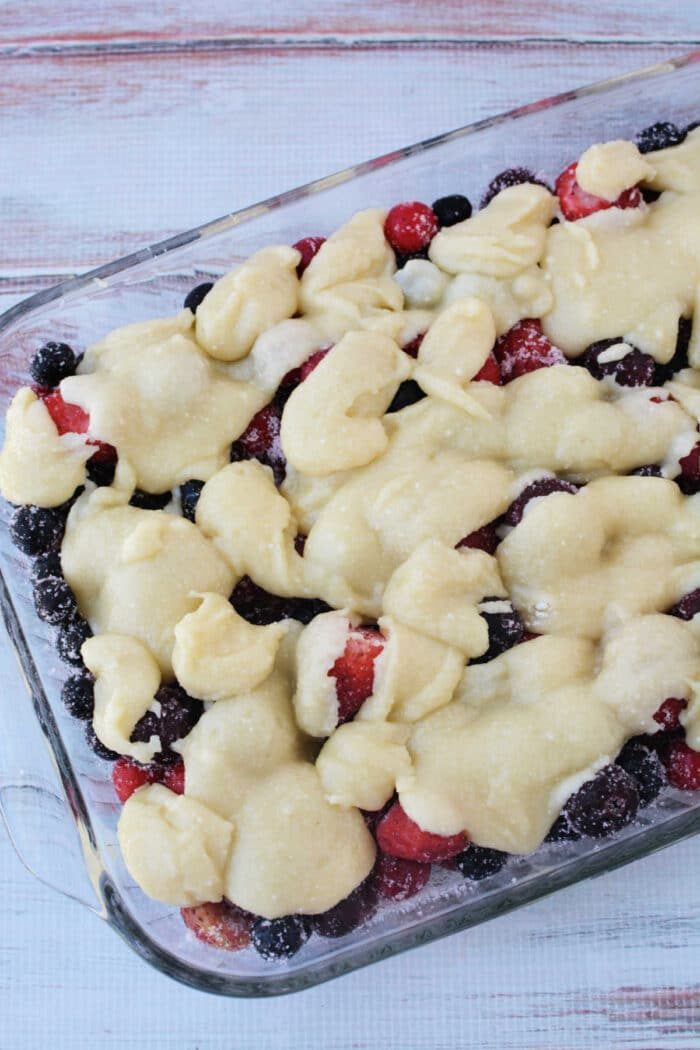 A glass baking dish filled with mixed berries and blobs of unbaked dough on top, this Berry Cobbler with Cake Mix is ready to be baked for a simple, good dessert.