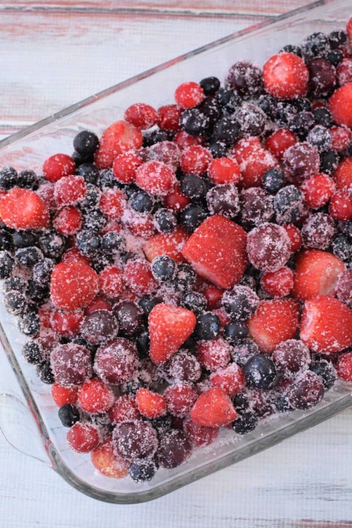 A glass dish filled with mixed frozen berries covered in sugar, ready to become a good Berry Cobbler with Cake Mix.