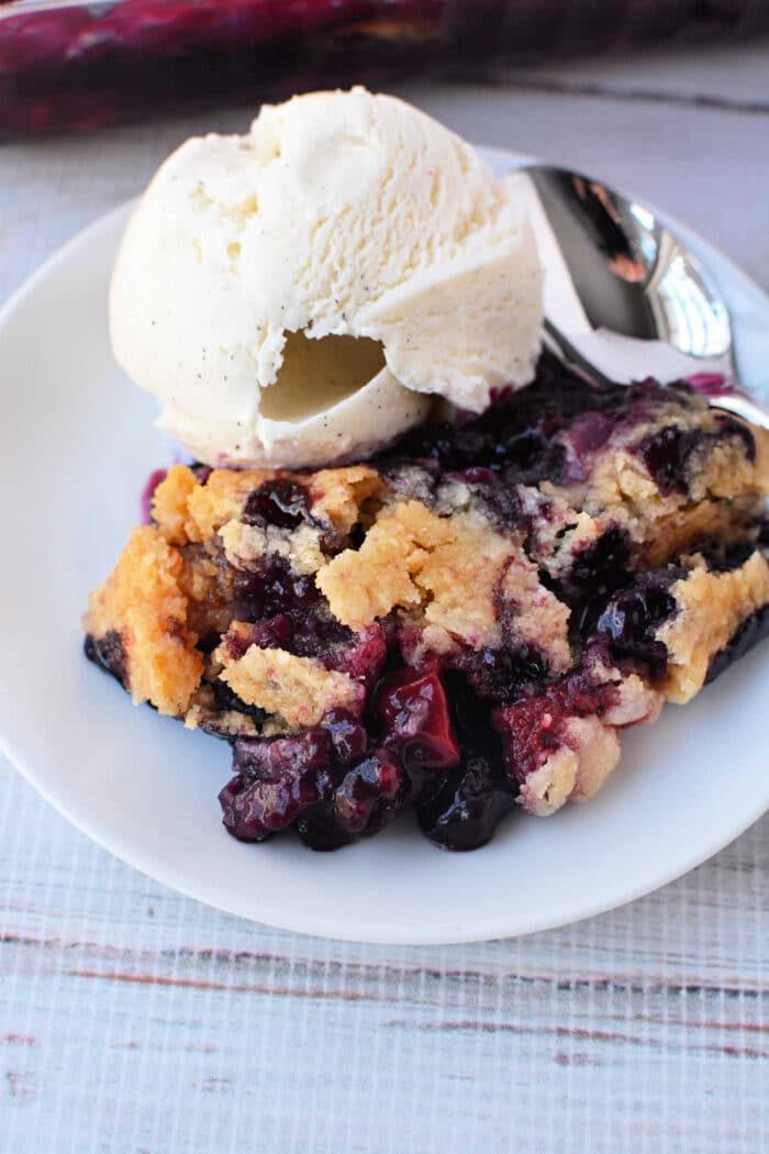 A plate with Berry Cobbler with Cake Mix and a scoop of vanilla ice cream, with a spoon beside them.