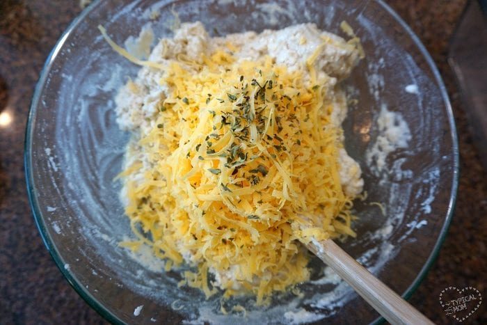 A bowl with shredded cheese and herbs crowns the best beer bread recipe. A wooden spoon rests elegantly in the dough mixture, ready to craft this good masterpiece.