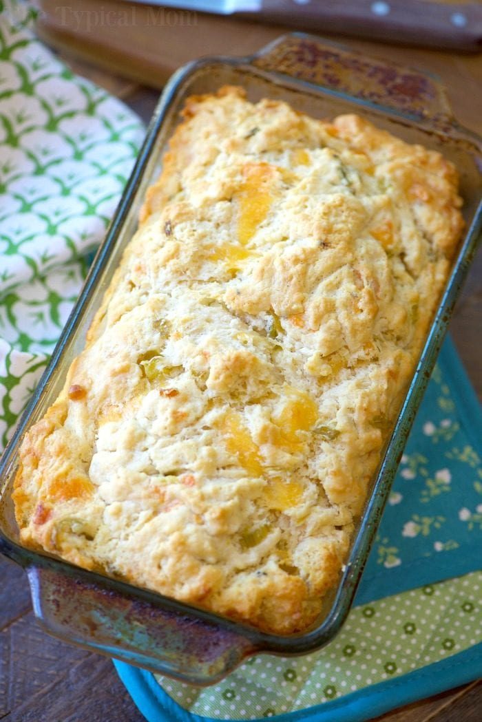 A loaf of good beer bread, reminiscent of the best beer bread recipe, sits invitingly in a glass baking dish, with floral and teal cloths underneath.