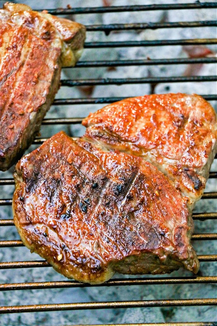 Two pieces of grilled steak on a metal grate, showcasing solid grill marks and a browned finish—a testament to the best grilled steak recipe.