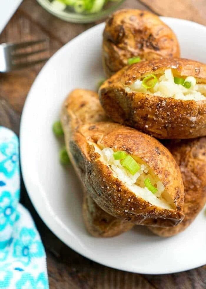 Baked potatoes without foil topped with chopped green onions on a white plate.