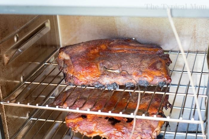 Two racks of seasoned ribs cooking smoker, placed on separate wire shelves – a method hailed by many as the best way to smoke ribs indoors.