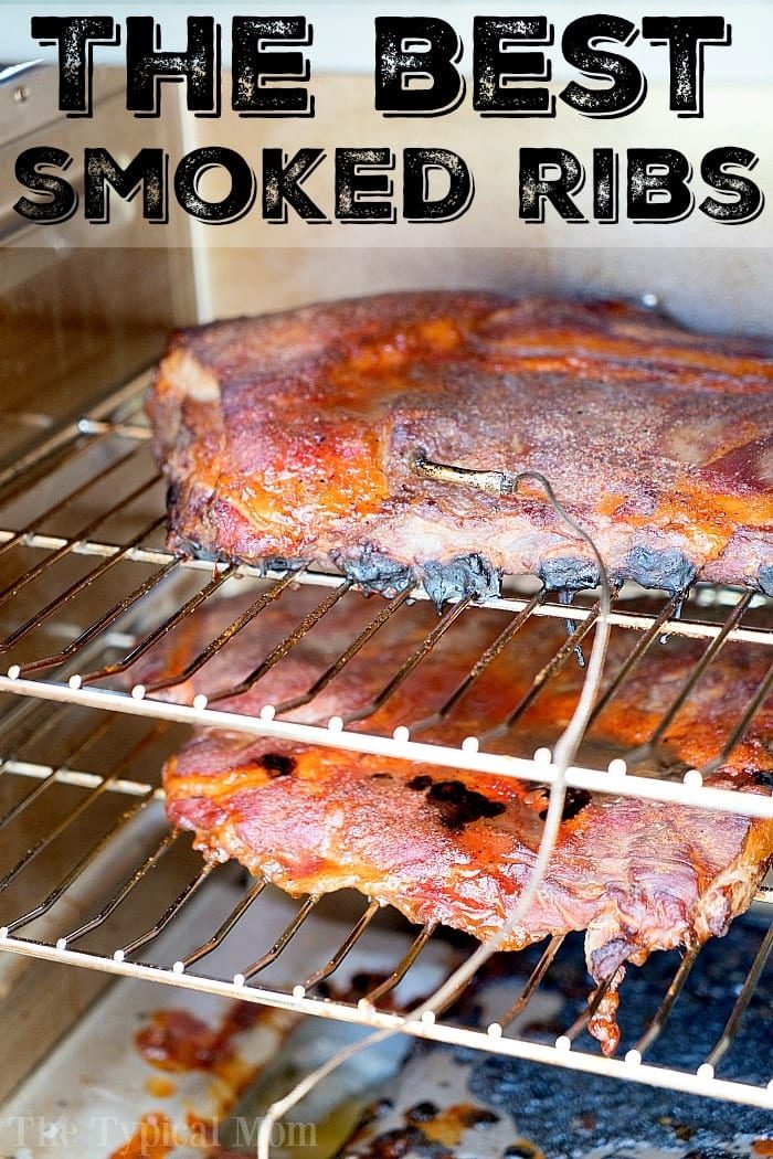 Smoked ribs cooking in smoker, topped with seasoning and a meat thermometer inserted—truly the best way to smoke ribs to perfection.