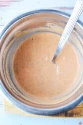 A metal bowl of creamy pink sauce, solid for drizzling over Big Mac Sloppy Joes, sits with a spoon on a wooden surface.