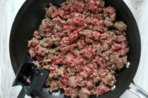 Ground beef being browned in a black skillet with a black spatula resting on the side—solid for an easy sloppy joe recipe 3 ingredients or less.