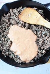 Ground beef simmered in a creamy, Big Mac-inspired sauce, mingling with sautéed onions in a skillet. A wooden spatula rests nearby, ready to serve these delightful Sloppy Joes.