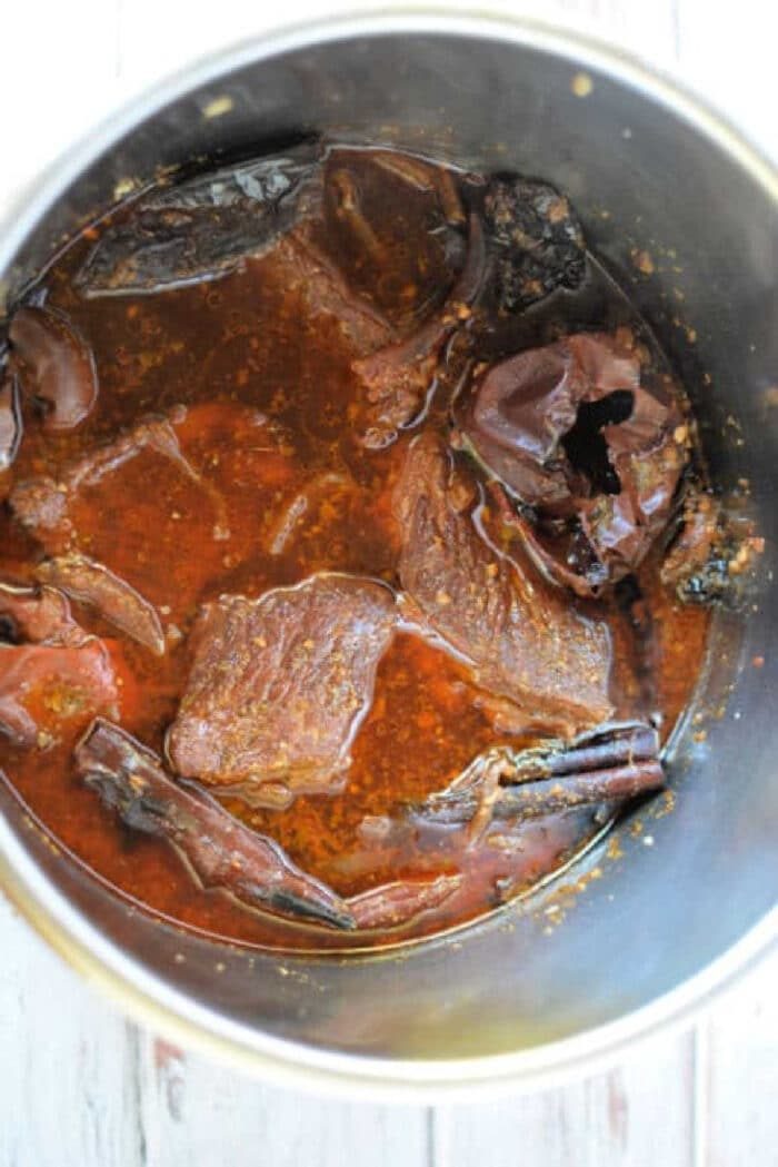 A pot of savory cooked birria red sauce and spices, solid for making mouthwatering Birria Quesadillas.