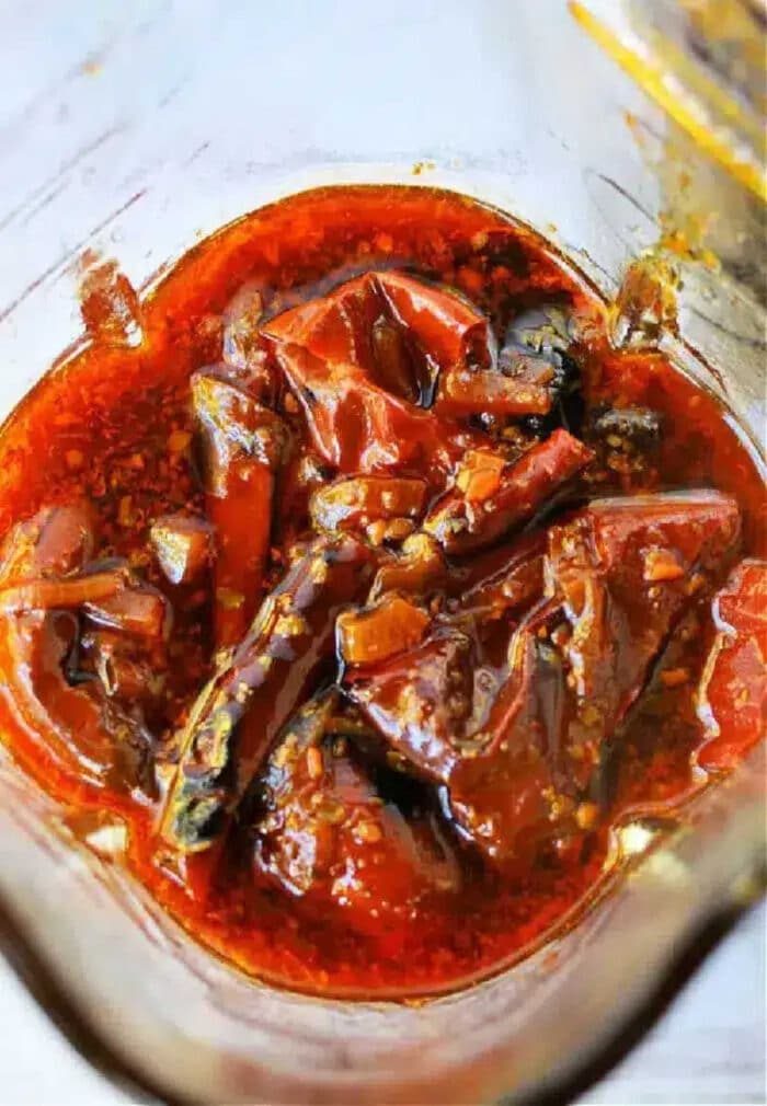 Red chili pickle soaked in oil and spices, with visible whole red chilies and seeds in a glass jar—solid as a fiery Birria Tacos Sauce or zesty condiment.