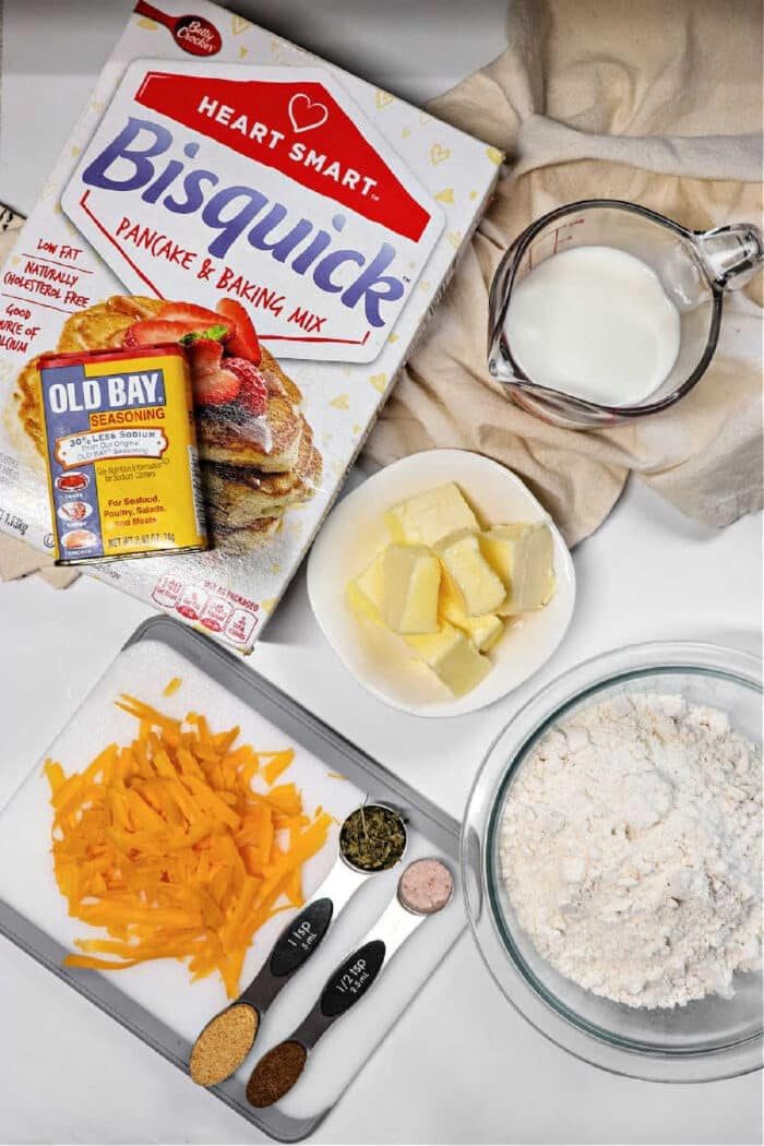 Bisquick cheddar bay biscuits ingredients—cheddar cheese, spices, butter, flour, and milk—are arranged on a counter for baking.